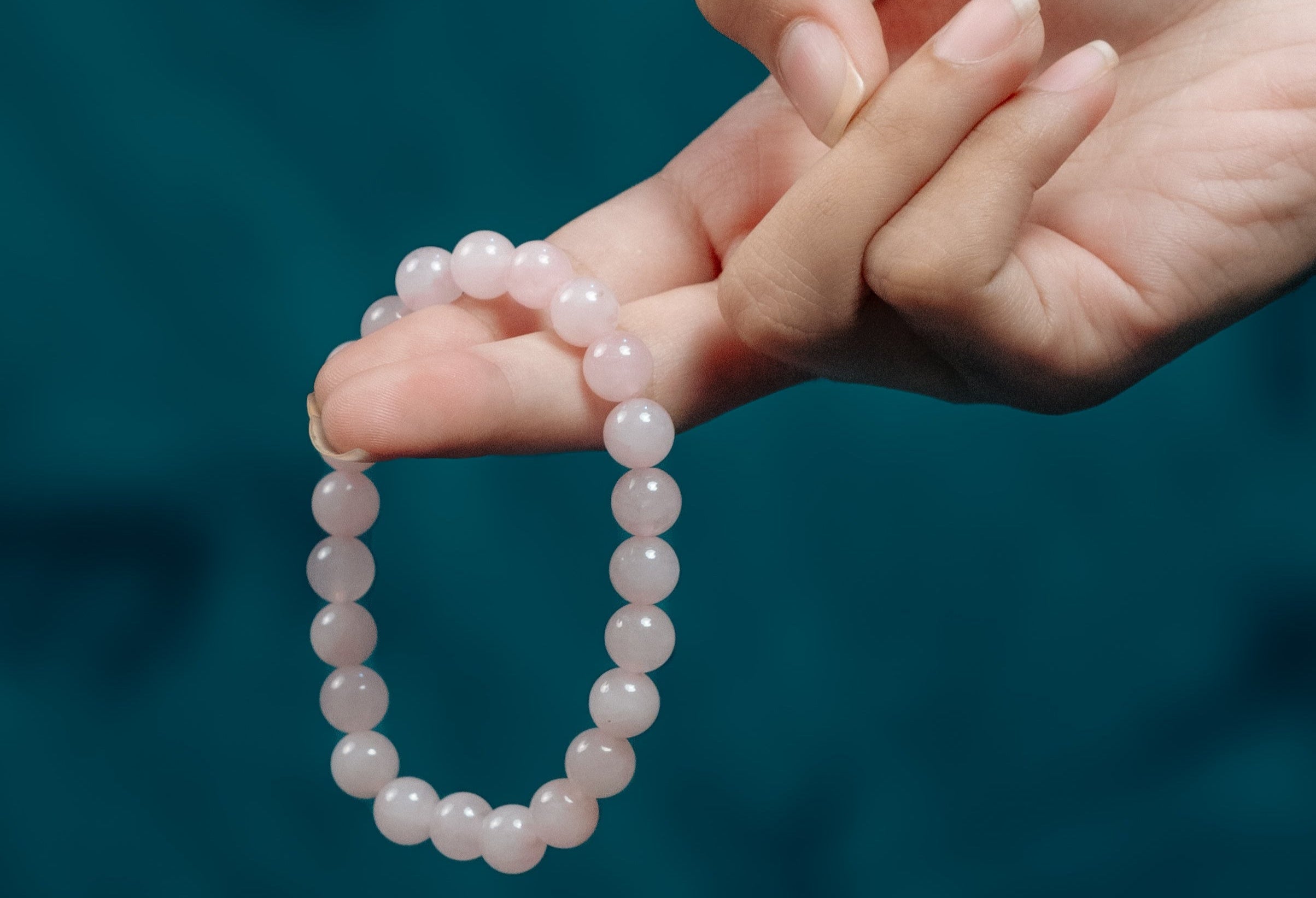 Hand holding a pink beaded bracelet against a blurred blue background